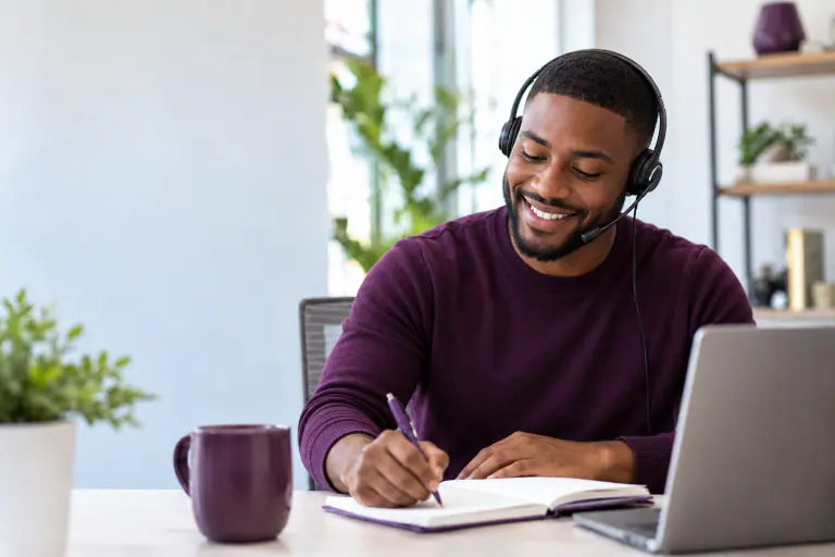 Rep on a headset mid call, writing notes, smiling
